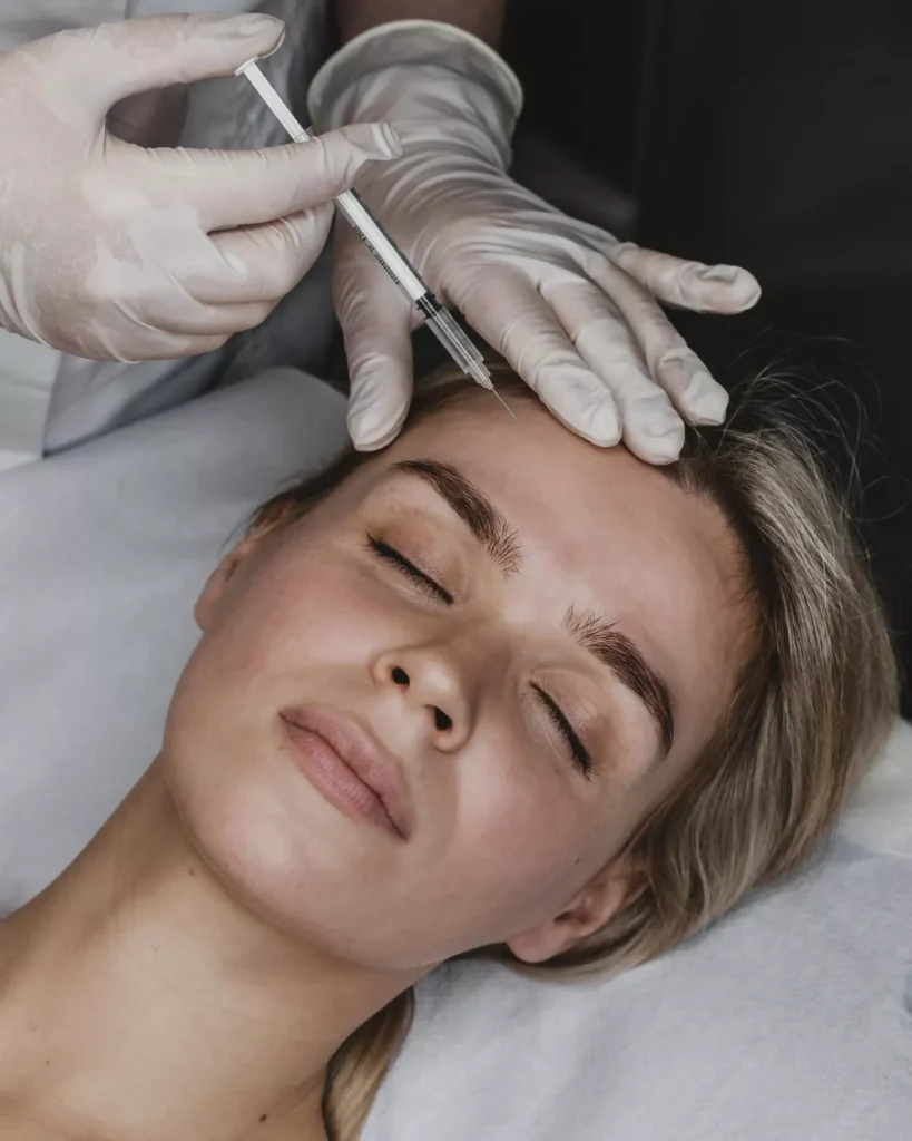 Home 8 Paciente recebendo aplicação de plasma rico em fibrina (PRF) na face para rejuvenescimento e harmonização facial, com profissional utilizando luvas rosas para garantir a higiene e precisão do procedimento.